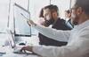 a man points with his pen at a monitor while a coworker looks